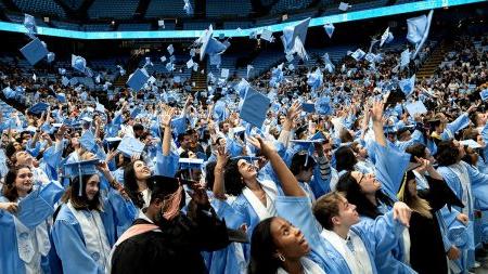 Graduates of U.N.C Chapel Hill in regalia throwing up their caps in Winter Commencement in the Dean E. Smith Center.